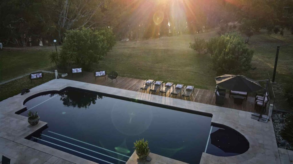 An overhead view of a pool at sunset with green grass, gumtrees and the Murray River in the background